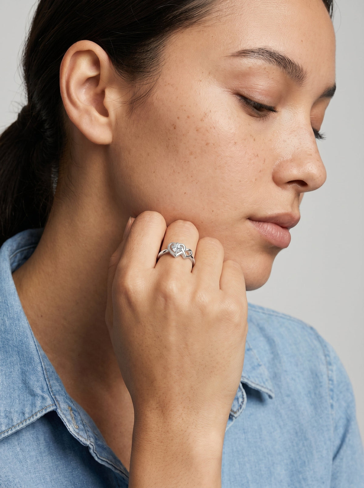Mujer con un anillo con una piedra preciosa azul en forma de corazón sobre un fondo neutro.