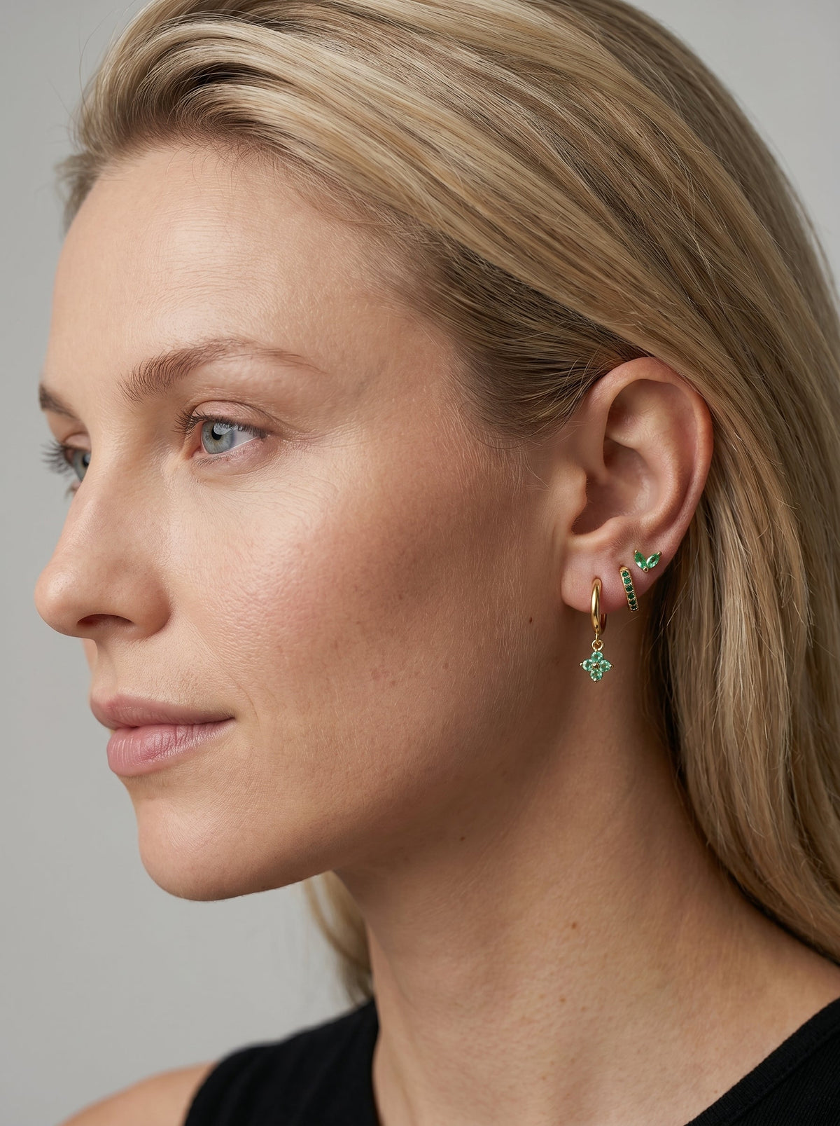 Primer plano de una mujer con pendientes verdes sobre un fondo neutro.