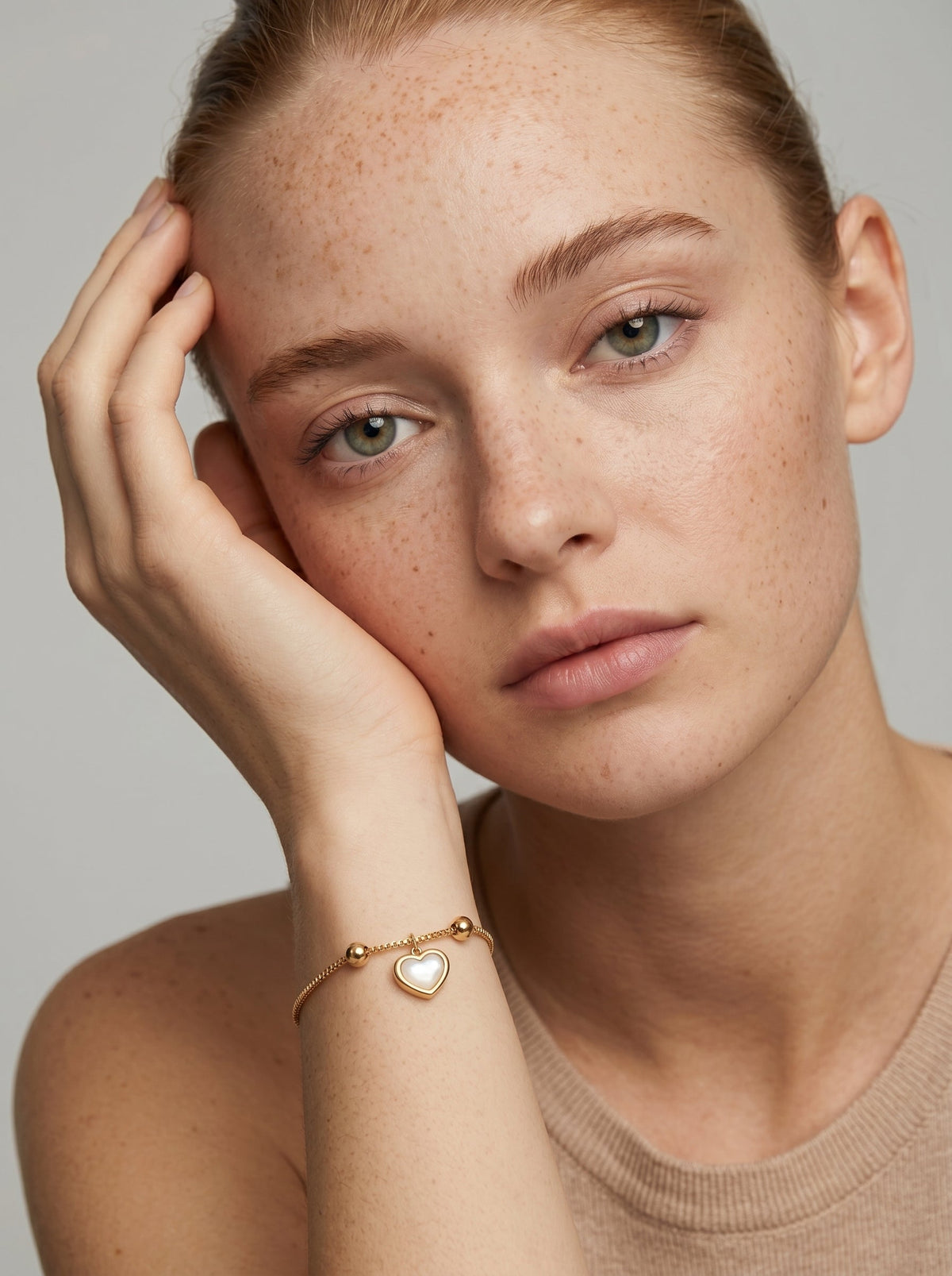Pulsera dorada delicada con colgante en forma de corazón blanco y acabado brillante, llevada por una modelo para un look elegante, femenino y romántico.