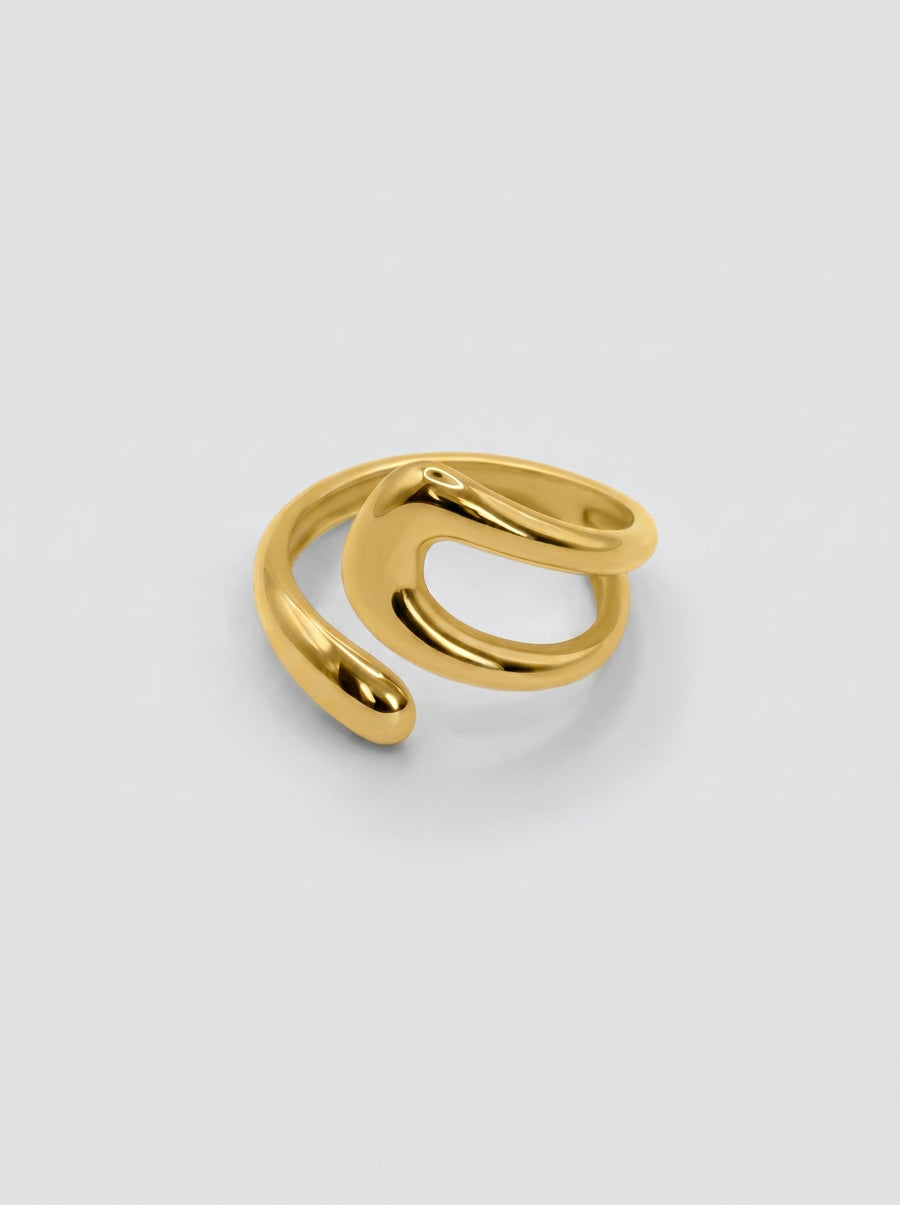 Anillo dorado ajustable de forma fluida y moderna, con superficie pulida y diseño abierto sobre fondo neutro.