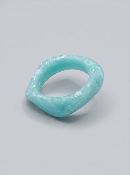 Pulsera Agua de Mar en resina marmoleada en tonos azul marino y turquesa, con diseño orgánico geométrico y acabado brillante, ideal para un look elegante y contemporáneo.
