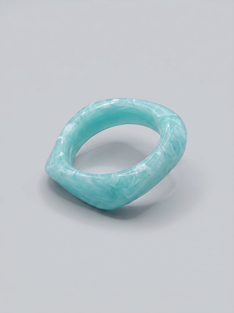 Pulsera Agua de Mar en resina marmoleada en tonos azul marino y turquesa, con diseño orgánico geométrico y acabado brillante, ideal para un look elegante y contemporáneo.
