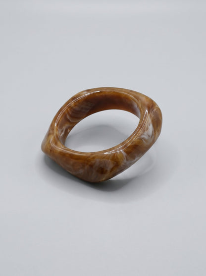 Pulsera Caramelo en resina marmoleada en tonos caramelo y dorado, con diseño orgánico geométrico y acabado brillante, ideal para un look elegante y contemporáneo.
