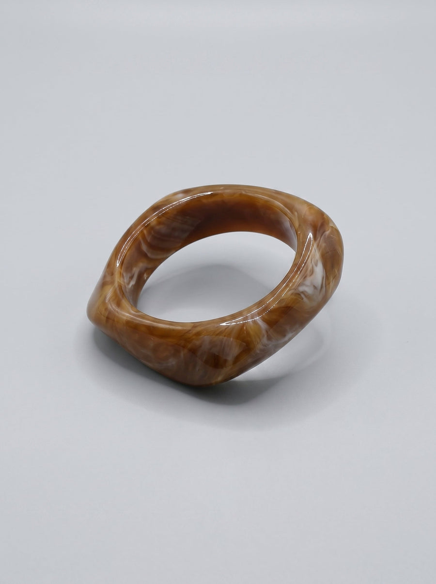 Pulsera Caramelo en resina marmoleada en tonos caramelo y dorado, con diseño orgánico geométrico y acabado brillante, ideal para un look elegante y contemporáneo.
