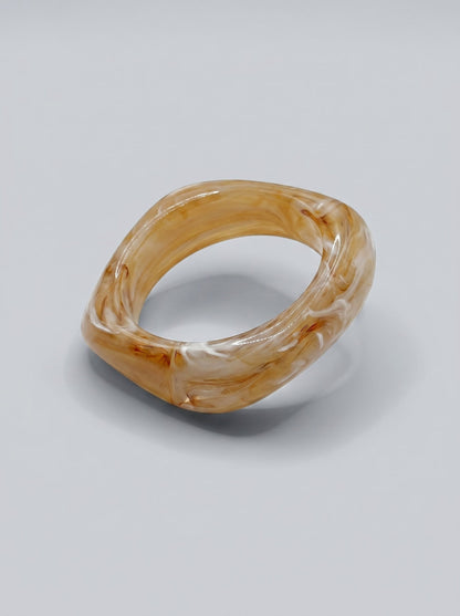 Pulsera Miel Silvestre en resina marmoleada en tonos miel y ámbar, con diseño geométrico orgánico y acabado brillante, ideal para un estilo elegante y contemporáneo.