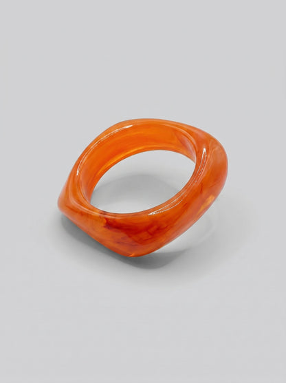 Pulsera Atardecer en resina marmoleada en tonos atardecer, coral y naranja, con diseño orgánico geométrico y acabado brillante, ideal para un look elegante y contemporáneo.