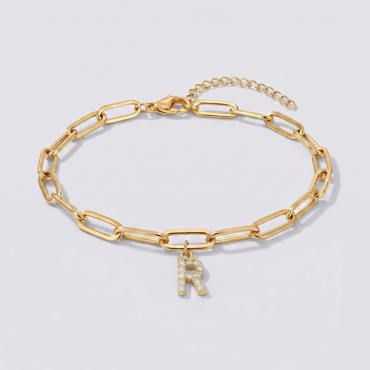 Pulsera dorada con letra inicial R, cadena paperclip y colgante de letra engastado.