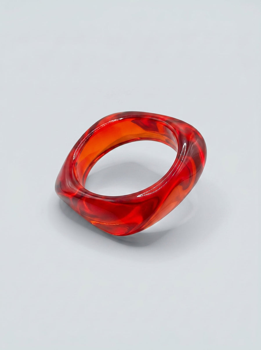 Pulsera Ruby de resina marmolada en tonos ruby y rojo intenso, con diseño orgánico geométrico y acabado brillante, ideal para un look elegante y contemporáneo.
