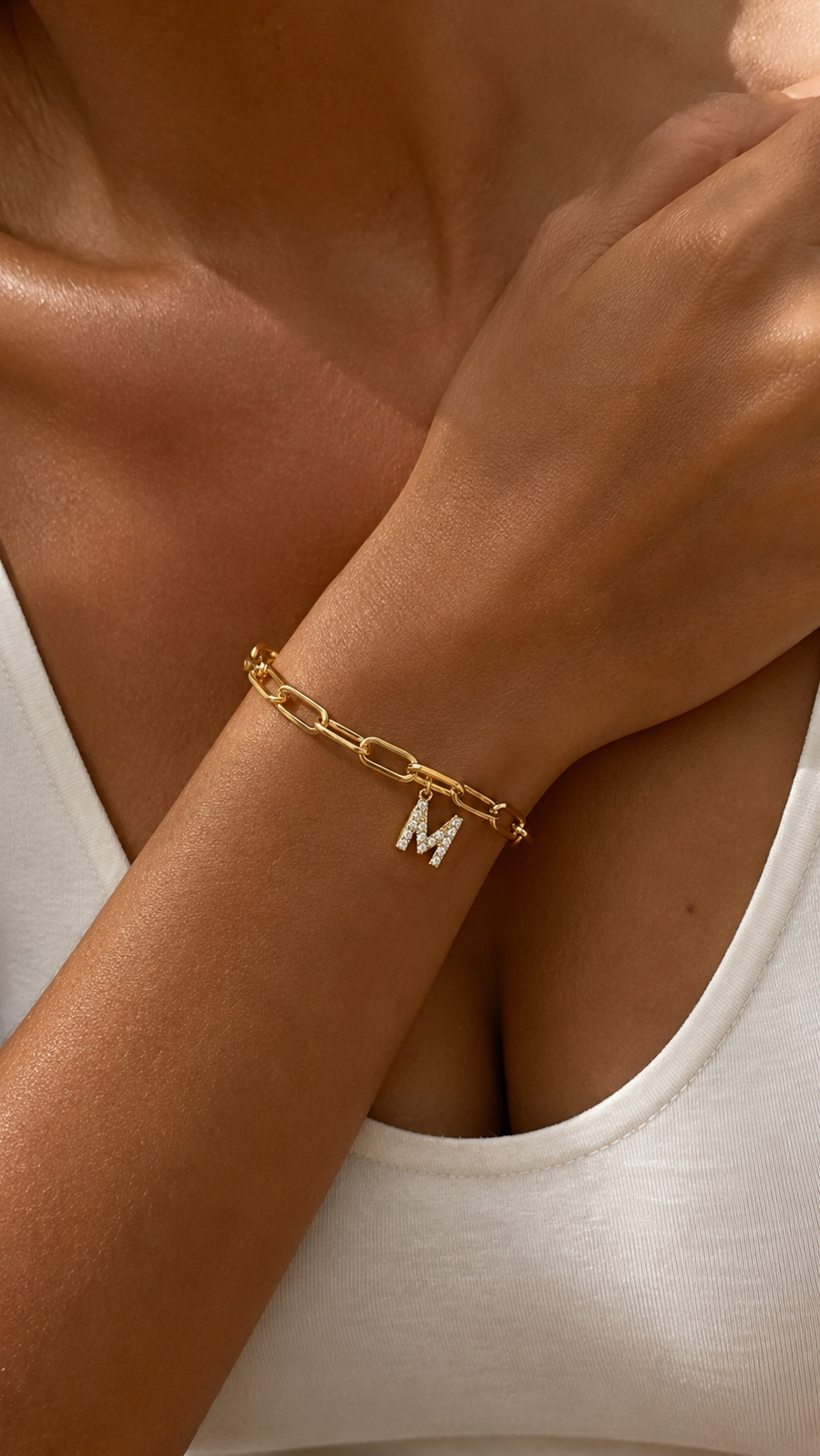 Pulsera dorada personalizada con inicial A, cadena paperclip y colgante de letra engastado en la muñeca femenina.