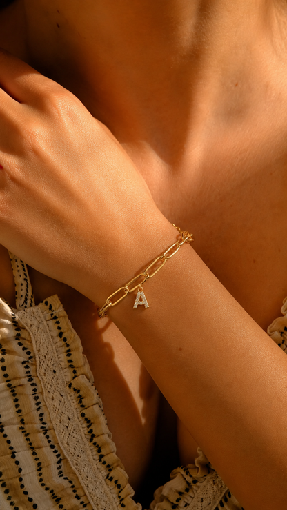 Pulsera dorada personalizada con inicial A, cadena paperclip y colgante de letra engastado en la muñeca femenina.