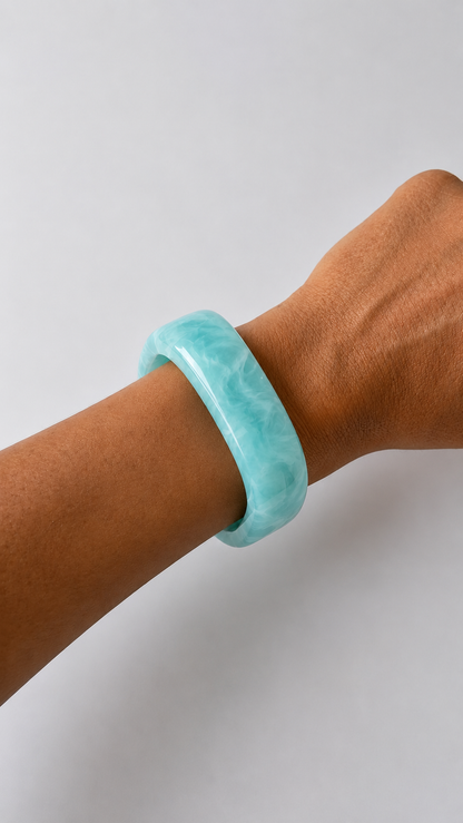 Pulsera de resina azul turquesa usada en la muñeca, con acabado brillante y estilo elegante.
