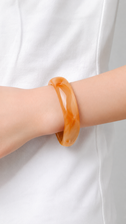 Pulsera de resina naranja marmoleada usada en la muñeca, con acabado brillante y estilo elegante.