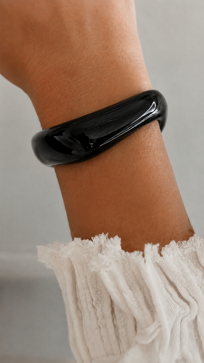 Pulsera de resina negra usada en la muñeca, con acabado brillante y estilo elegante.