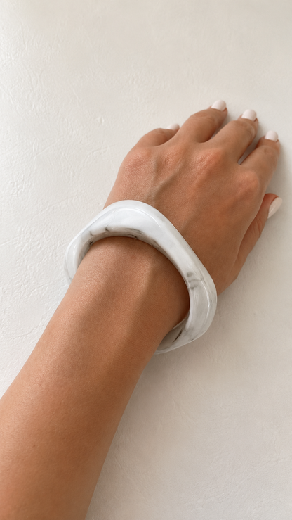 Pulsera de resina blanca marmoleada usada en la muñeca, con acabado brillante y estilo elegante.