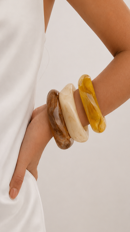 Pulseras de resina en marrón, beige y amarillo usadas en la muñeca, con diseño elegante y acabado brillante.