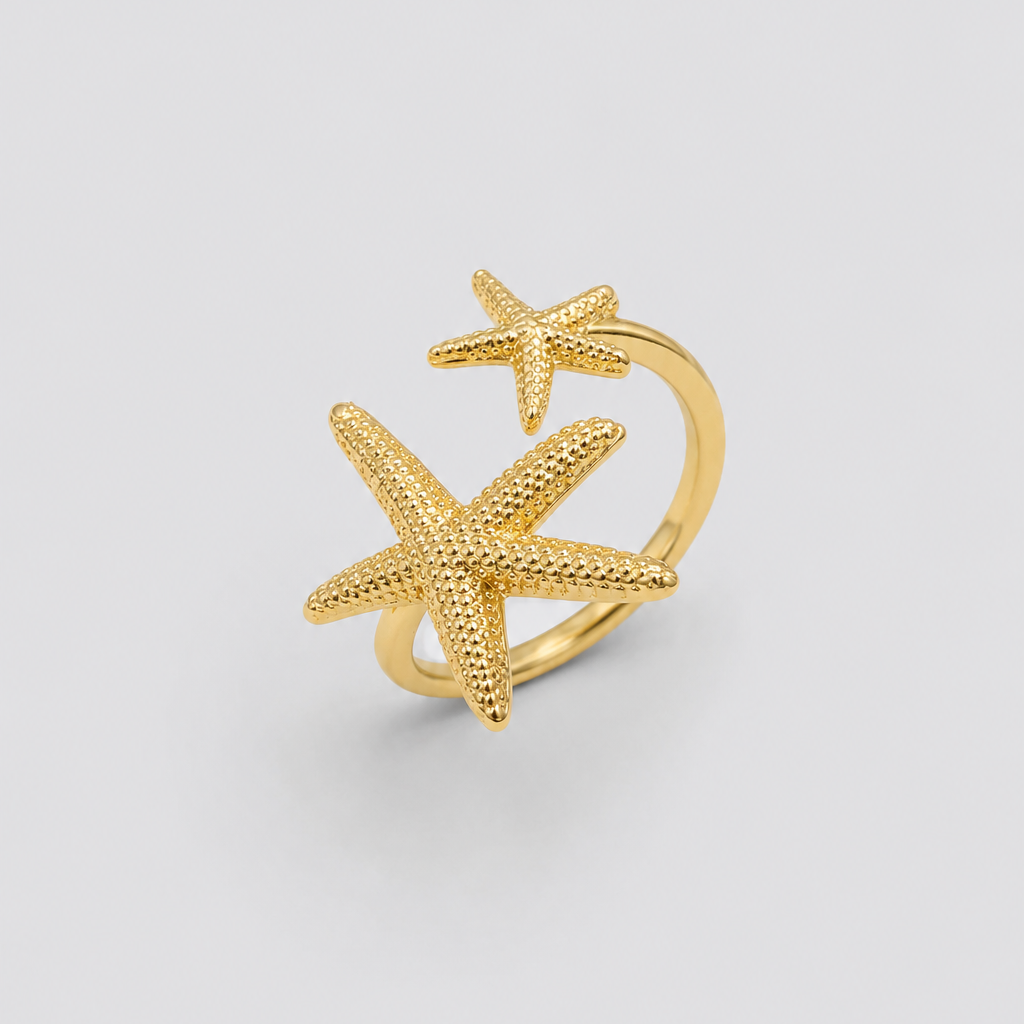 Anillo ajustable dorado con dos estrellas de mar texturizadas en tamaños diferentes, fotografiado sobre fondo gris claro para un look elegante, minimalista y sofisticado.