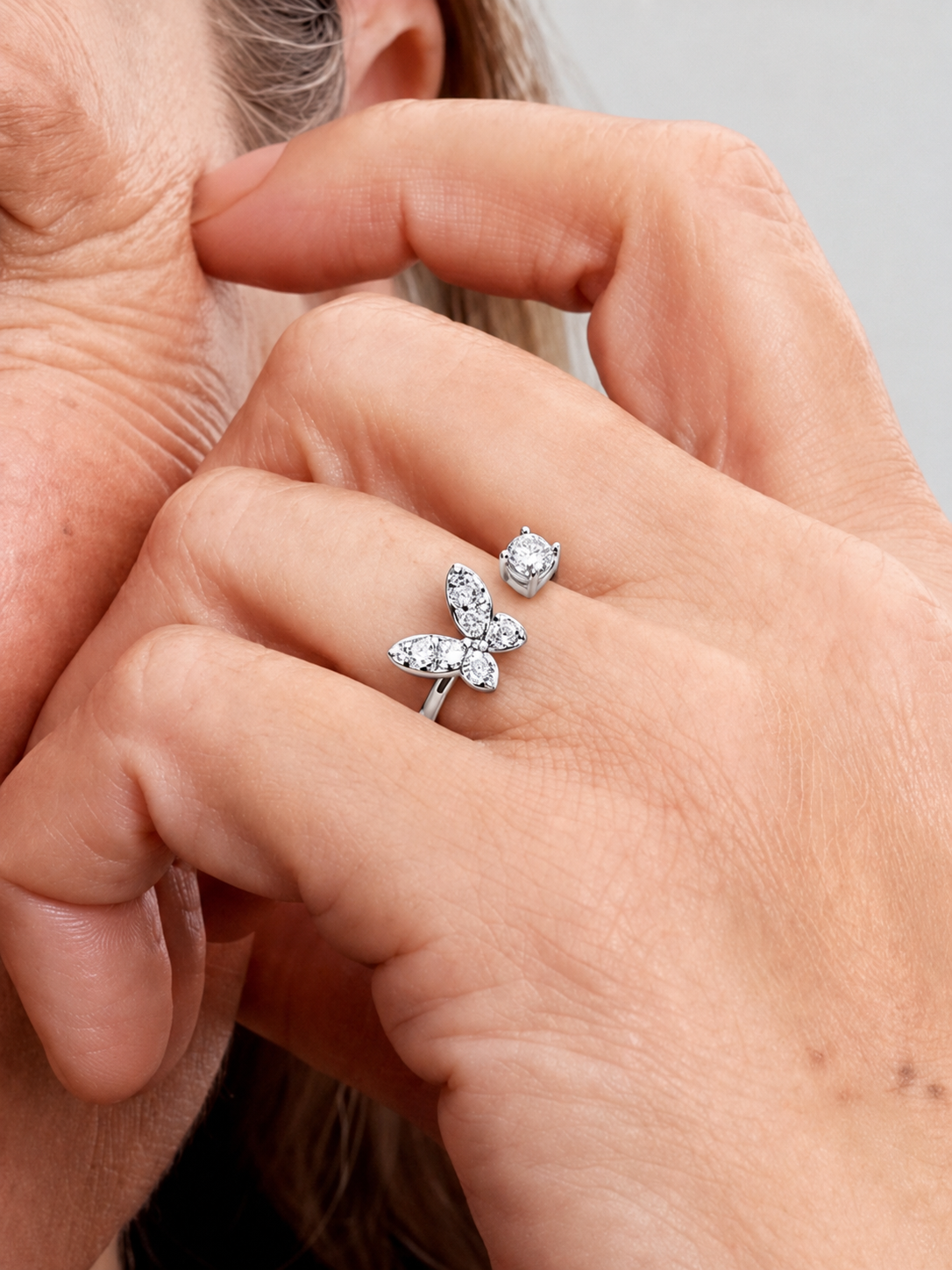 Detalle de una mano con un anillo de plata en forma de mariposa con pequeñas piedras.