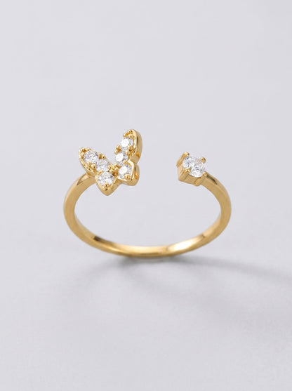 Anillo dorado con diseño de mariposa sobre fondo gris claro.
