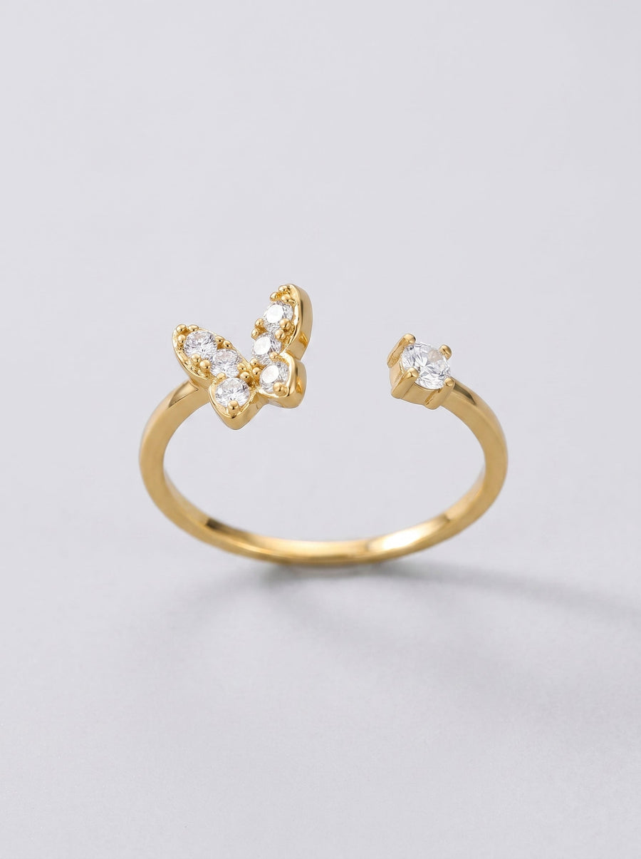 Anillo dorado con diseño de mariposa sobre fondo gris claro.