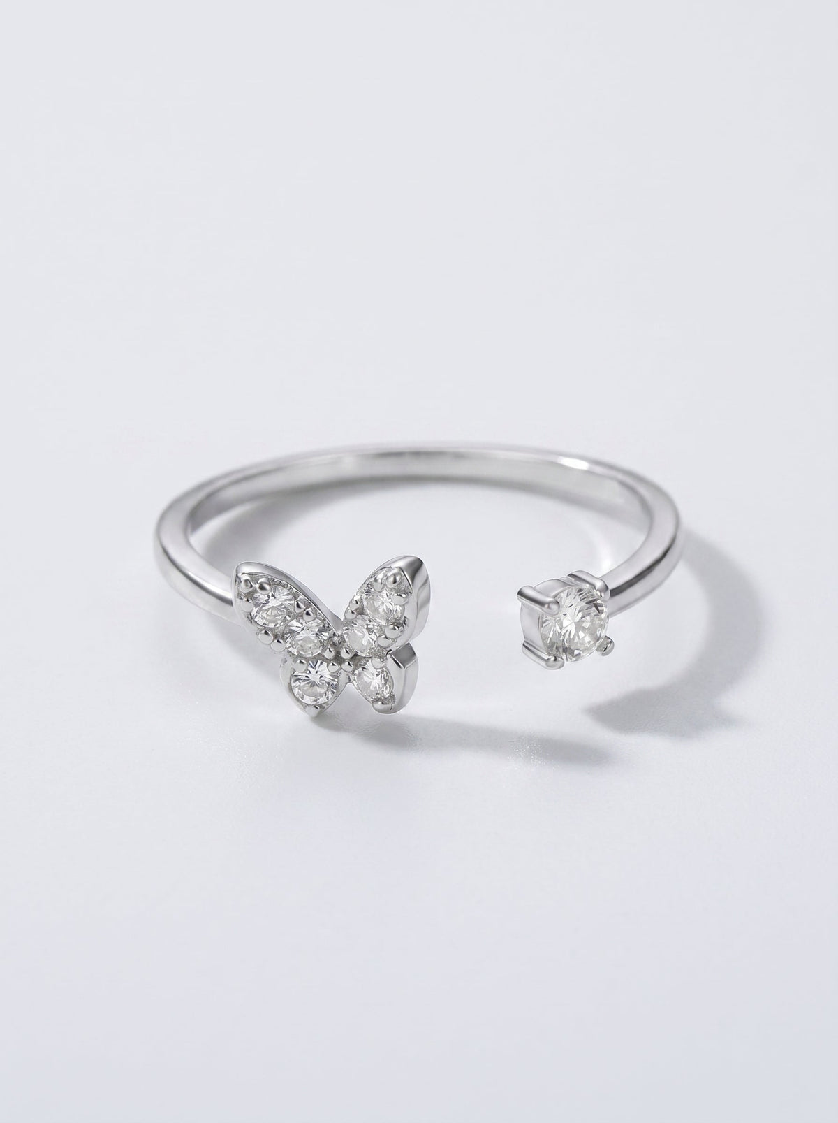 Anillo plateado con diseño de mariposa sobre fondo gris claro.