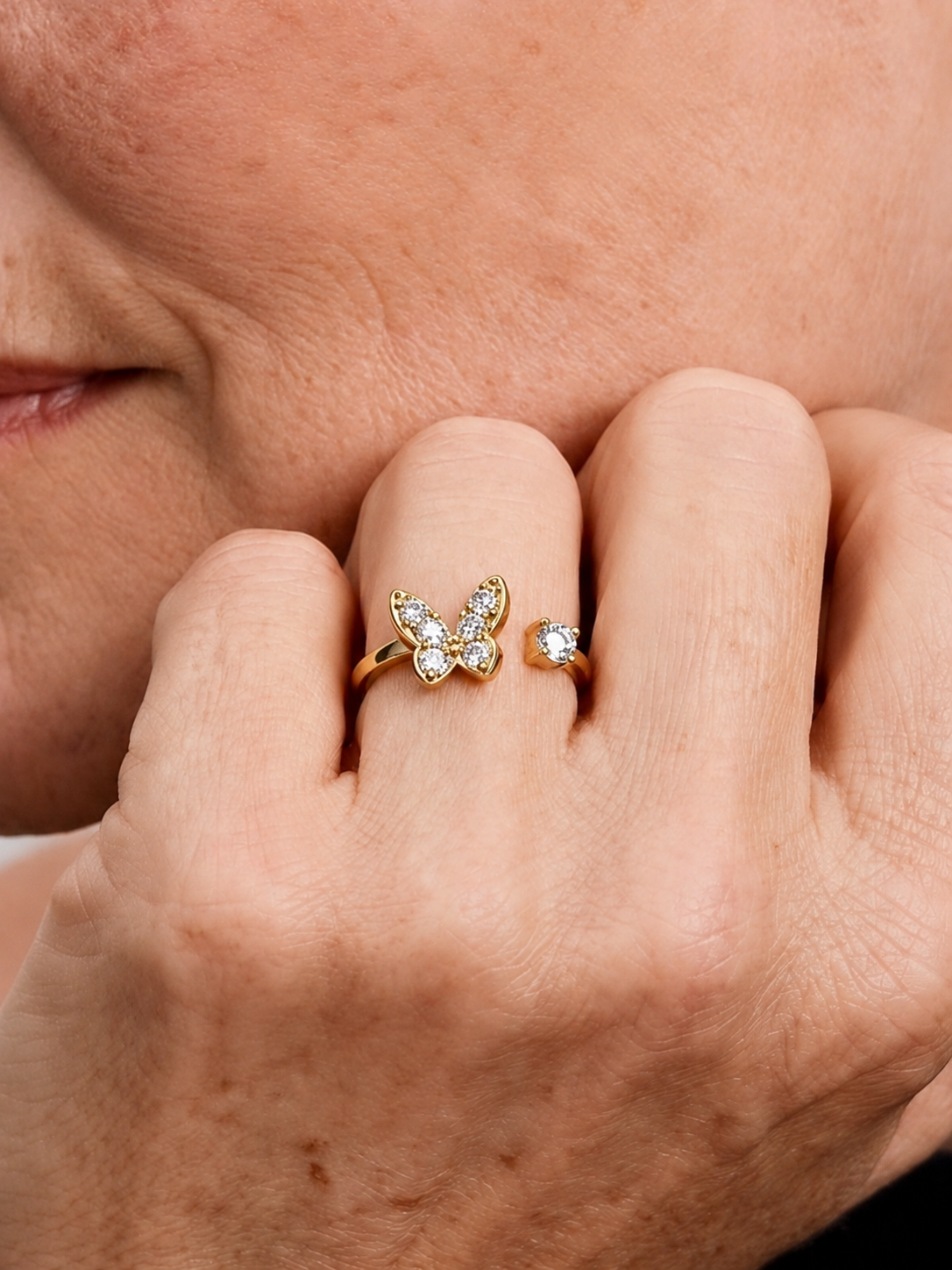 Detalle de una mano con un anillo de mariposa dorado con piedras transparentes.