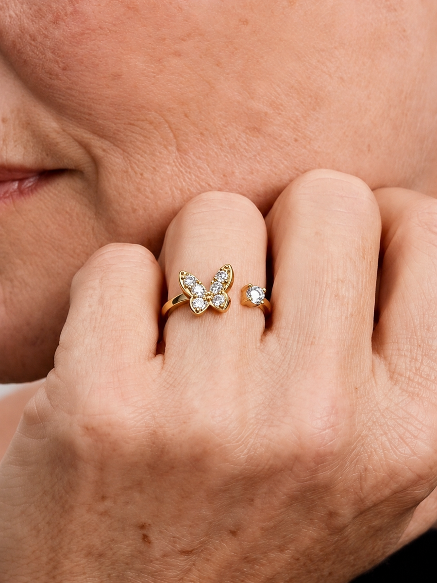Detalle de una mano con un anillo de mariposa dorado con piedras transparentes.