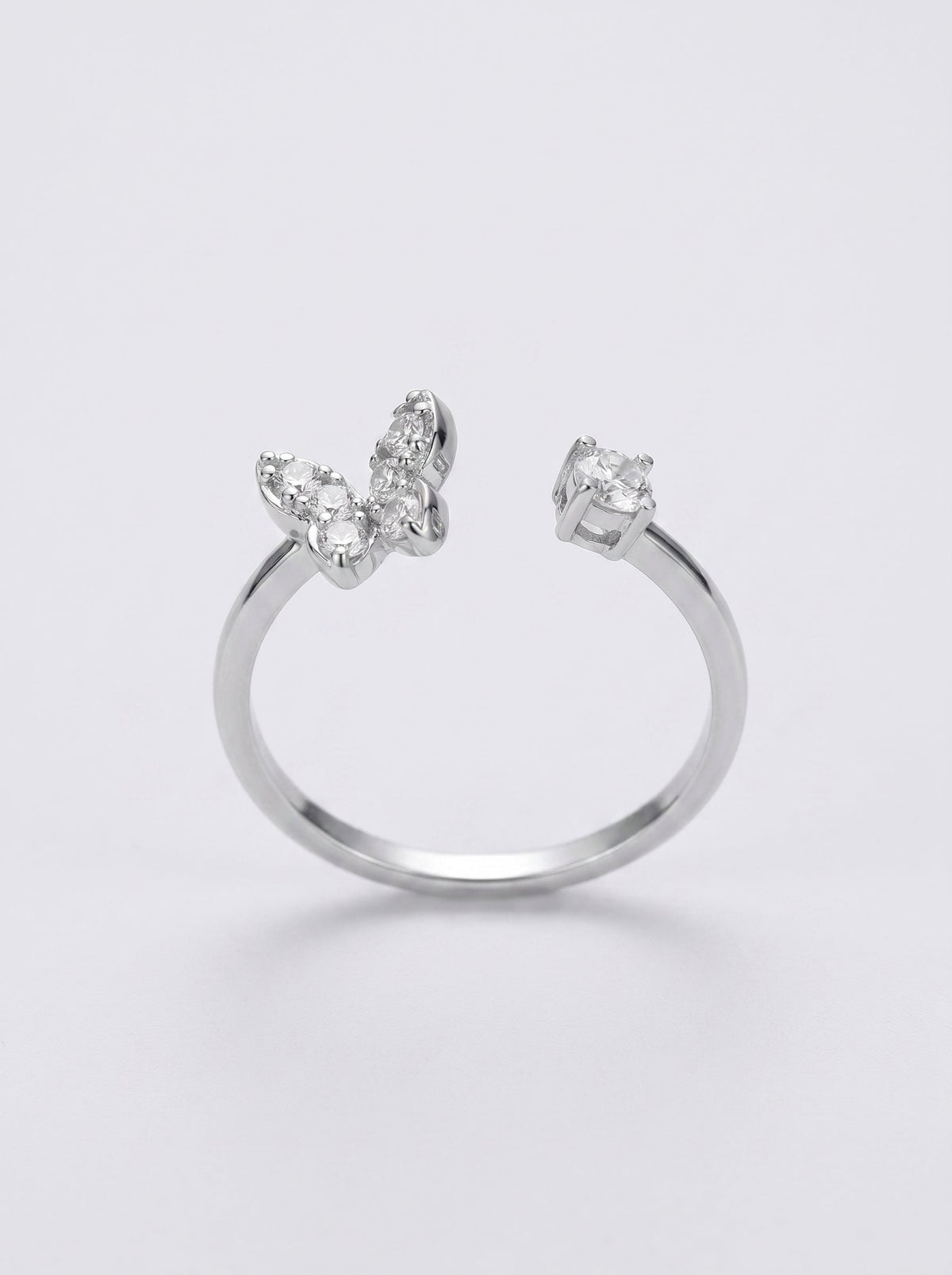 Anillo de plata con piedras en forma de mariposa sobre fondo gris claro.