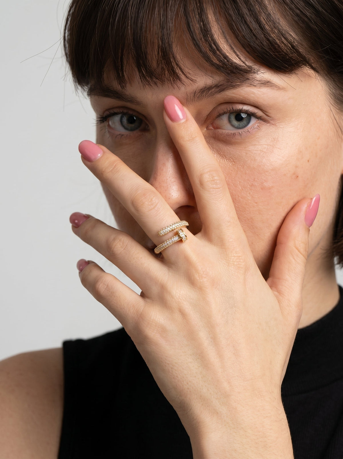 Mujer con un anillo y esmalte rosa sobre un fondo liso
