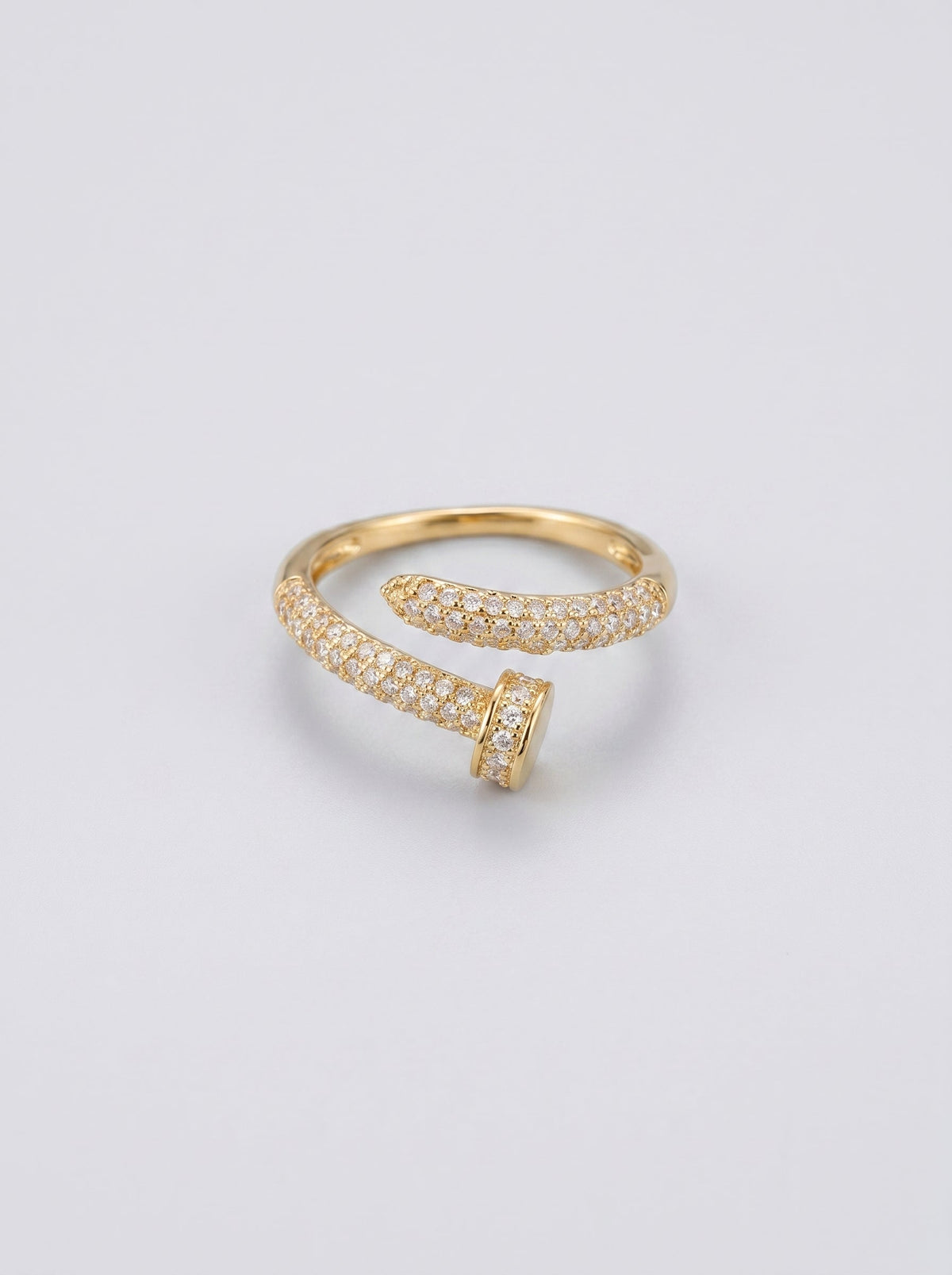 Anillo abierto dorado con pequeñas piedras sobre fondo gris claro.
