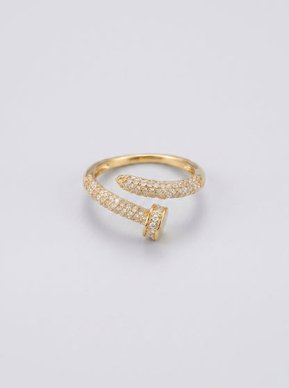 Anillo abierto dorado con pequeñas piedras sobre fondo gris claro.
