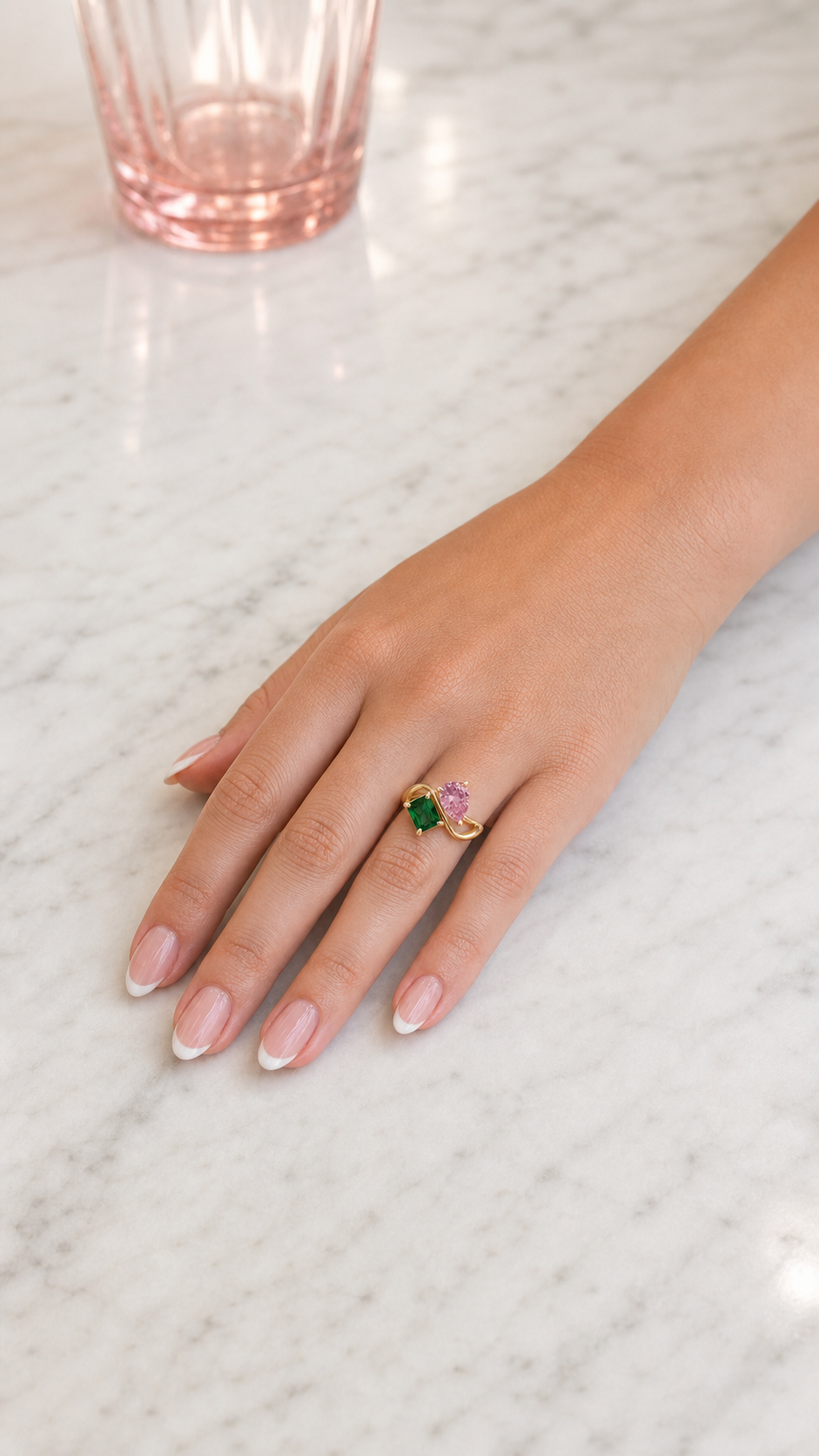 Mujer con anillo dorado con dos piedras de nacimiento — Octubre (Turmalina Rosa, pera) y Mayo (Esmeralda, rectángulo).