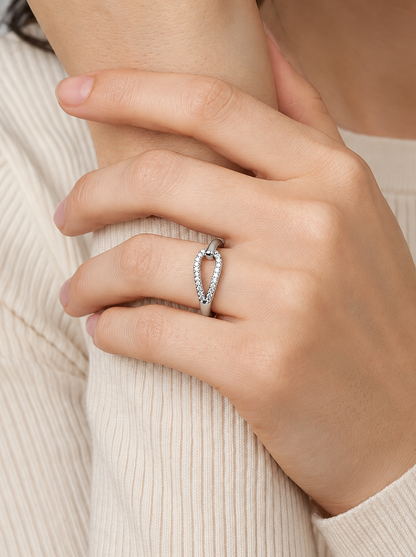 Mano con un anillo de plata con diseño de corazón sobre un fondo de tejido texturizado beige.