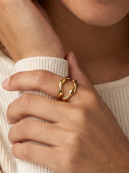 Anillo plateado con un diamante en forma de corazón sobre un fondo gris claro.
