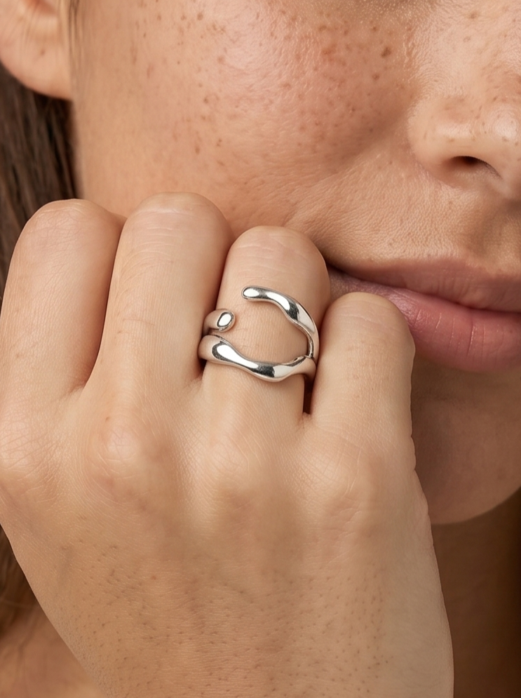 Primer plano de una persona con un anillo plateado con una pequeña perla sobre un fondo neutro.
