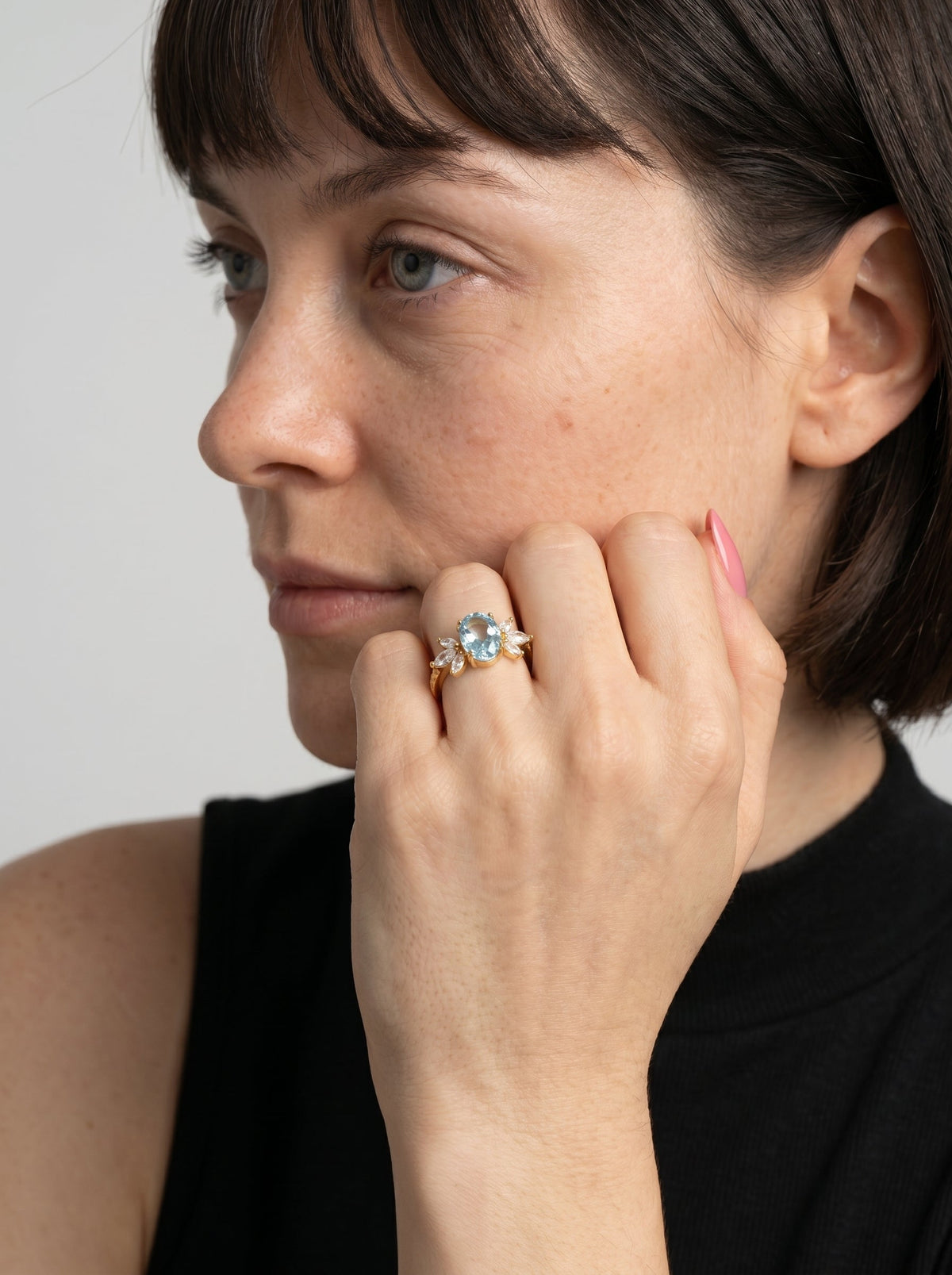 Mujer con un anillo de diamante en el dedo contra un fondo neutro.