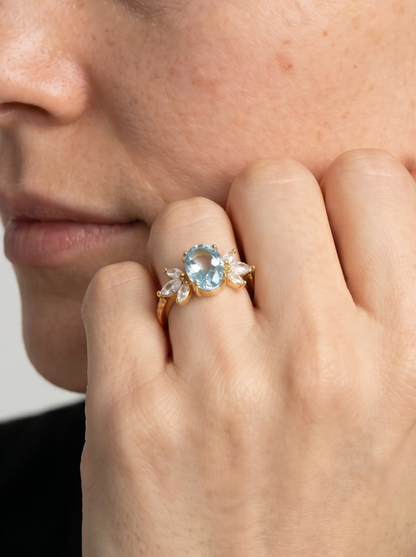 Primer plano de una mano con un anillo de piedra preciosa azul sobre un fondo neutro.