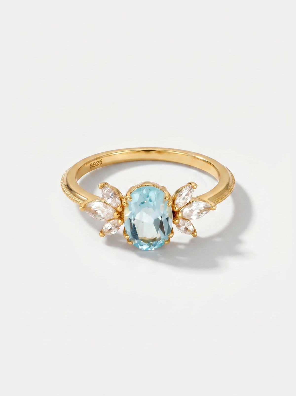 Anillo dorado con una piedra preciosa azul sobre un fondo gris claro.