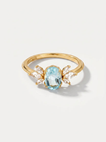 Anillo dorado con una piedra preciosa azul sobre un fondo gris claro.