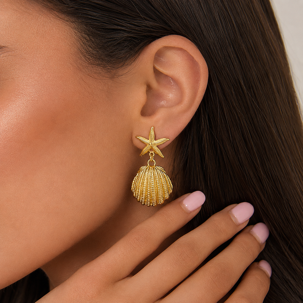 Pendientes dorados con estrella de mar y colgante de concha llevados en la oreja, para un look elegante, femenino y inspirado en el mar.