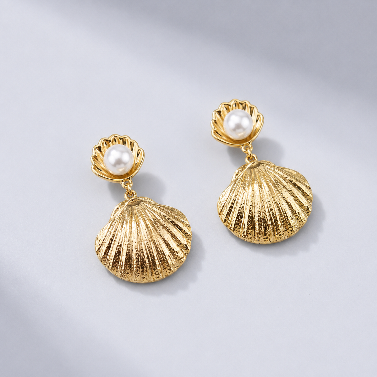 Pendientes dorados con concha y perla blanca y colgante de concha texturizada, fotografiados sobre fondo claro para un look elegante y femenino.