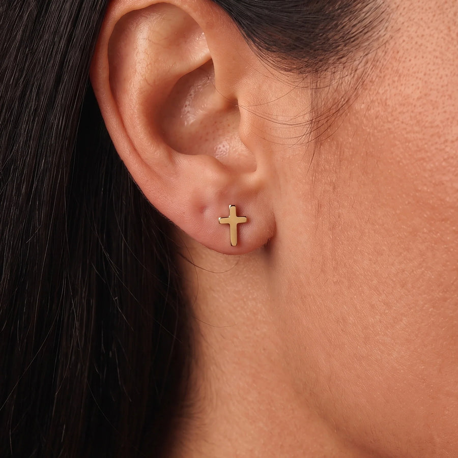 Pendientes cruz dorados en uso — primer plano en la oreja