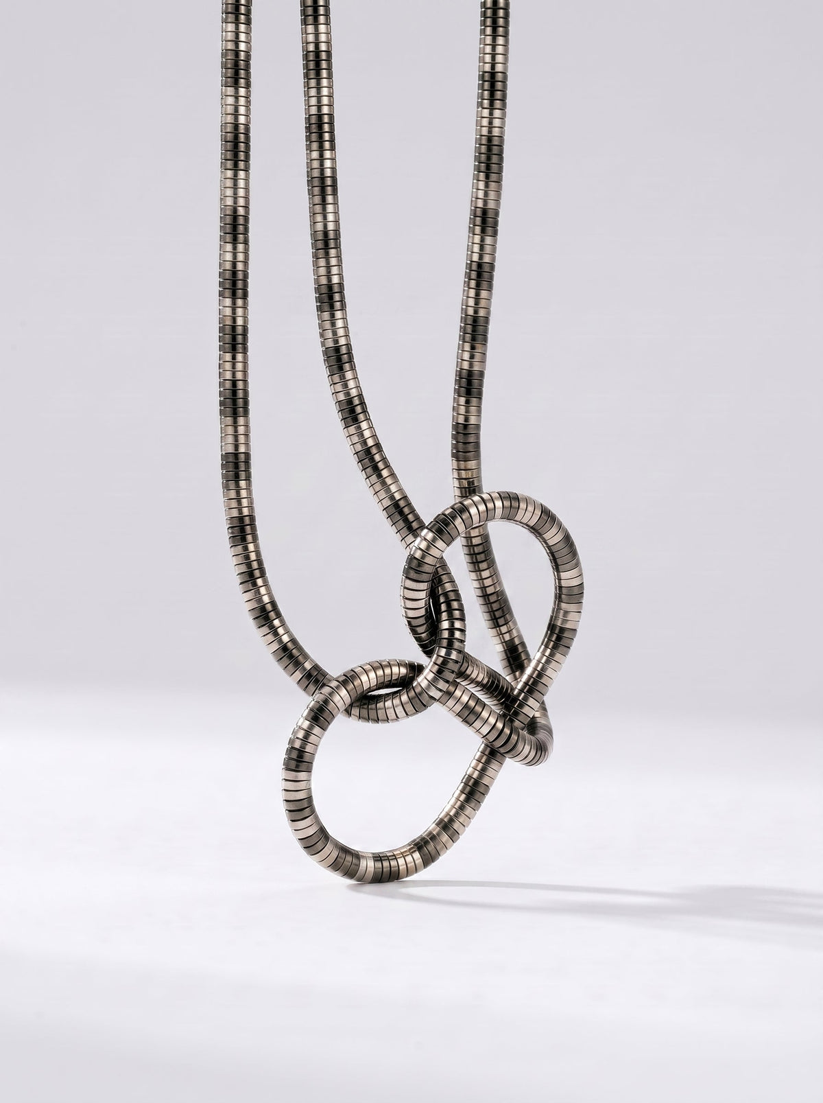 Collar plateado moderno con colgante abstracto en forma de nudo y acabado texturizado, fotografiado sobre fondo claro para un look elegante, artístico y sofisticado.