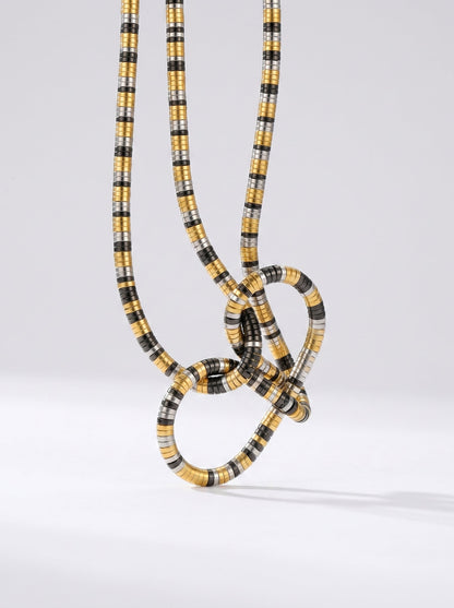 Collar bicolor en dorado, plateado y negro con colgante abstracto en forma de nudo y acabado texturizado, fotografiado sobre fondo claro para un look moderno, artístico y sofisticado.