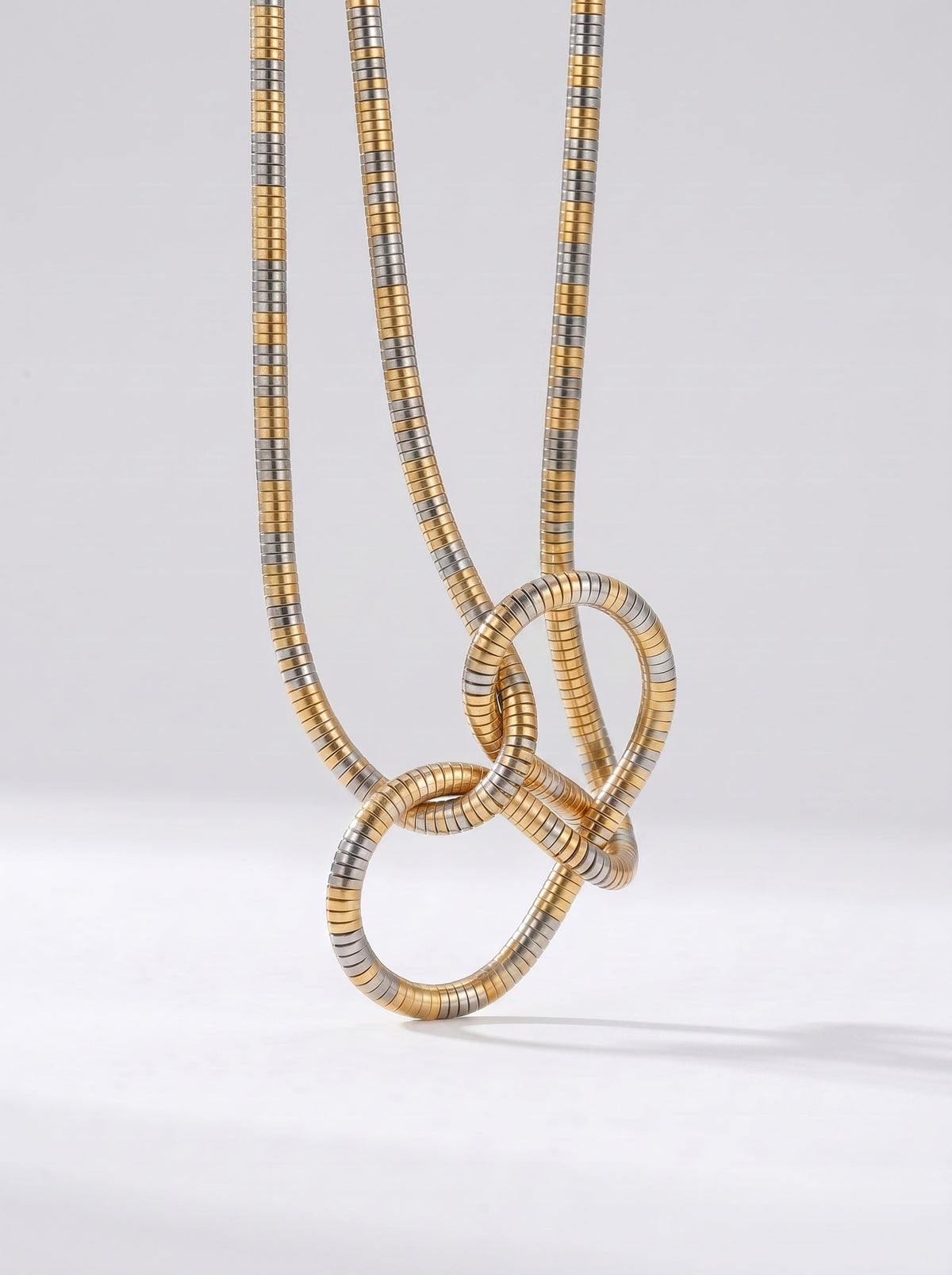 Collar bicolor en dorado y plateado con colgante abstracto en forma de nudo y acabado texturizado, fotografiado sobre fondo claro para un look moderno, artístico y sofisticado.
