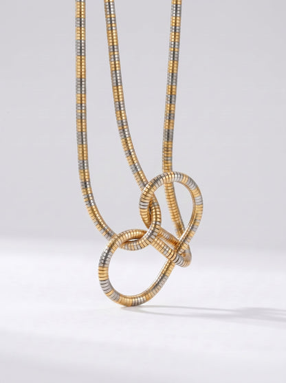 Collar bicolor en dorado y plateado con colgante abstracto en forma de nudo y acabado texturizado, fotografiado sobre fondo claro para un look moderno, artístico y sofisticado.