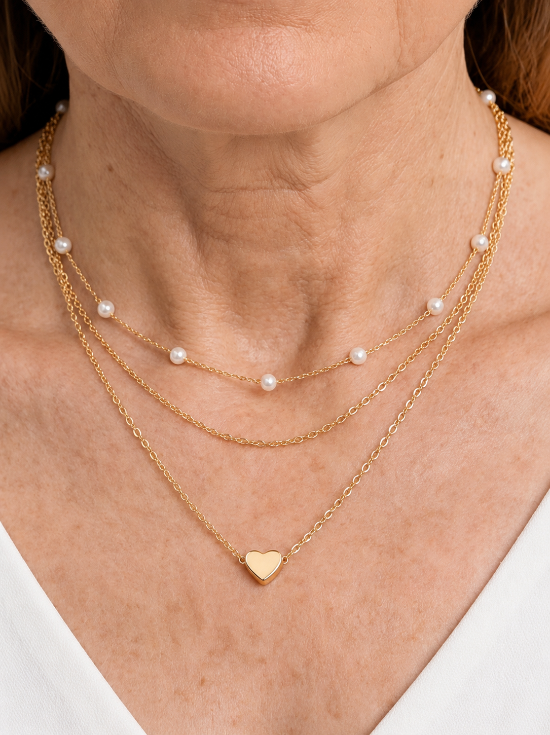 Collar dorado delicado en capas con perlas blancas y colgante en forma de corazón, usado al cuello para un look elegante, romántico y sofisticado.
