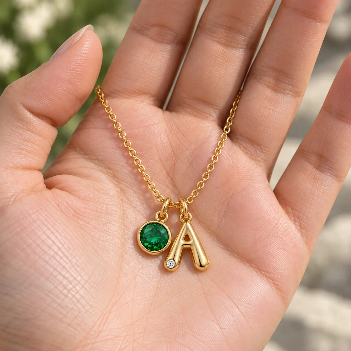 Collar Inicial A dorado con piedra Esmeralda mostrado en la mano