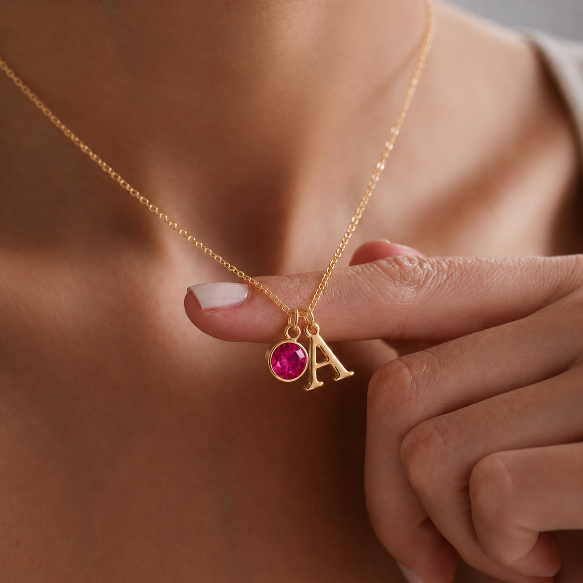 Primer plano de collar dorado con inicial A y piedra de nacimiento rosa, sujeto con la mano para destacar los detalles personalizados.