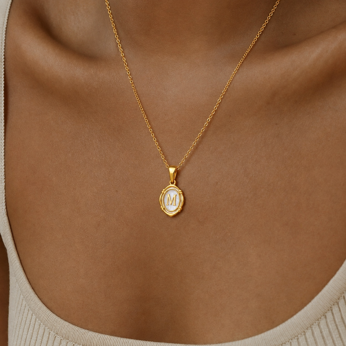 Mujer luciendo collar oval dorado personalizado con inicial M en nácar sobre el cuello.