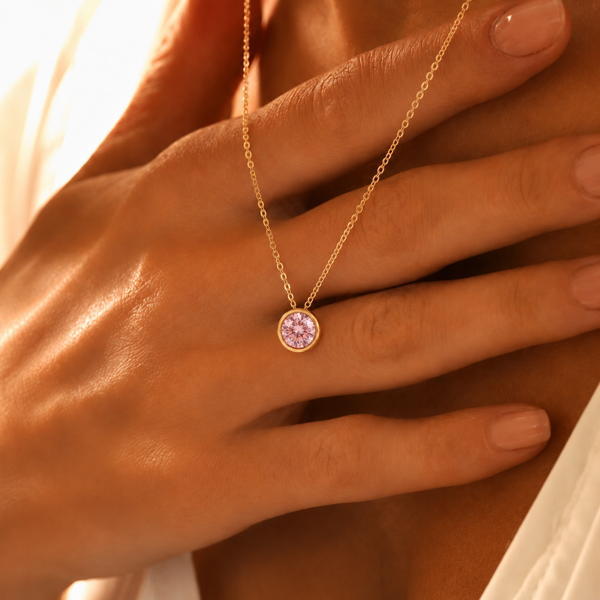 Mujer luciendo collar dorado con piedra de nacimiento rosa (Turmalina rosa) en el pecho, con la mano junto a la clavícula.